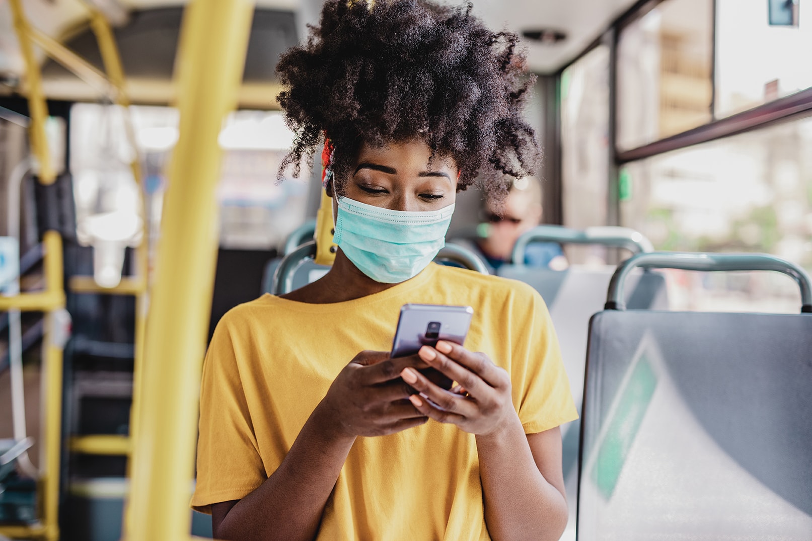 Girl with mask looking at phone on public transport 1